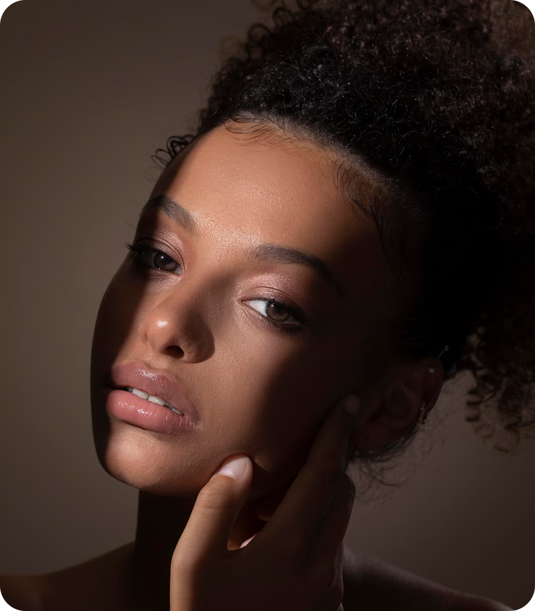 Close-up of a woman with her hand near her face against a brown background