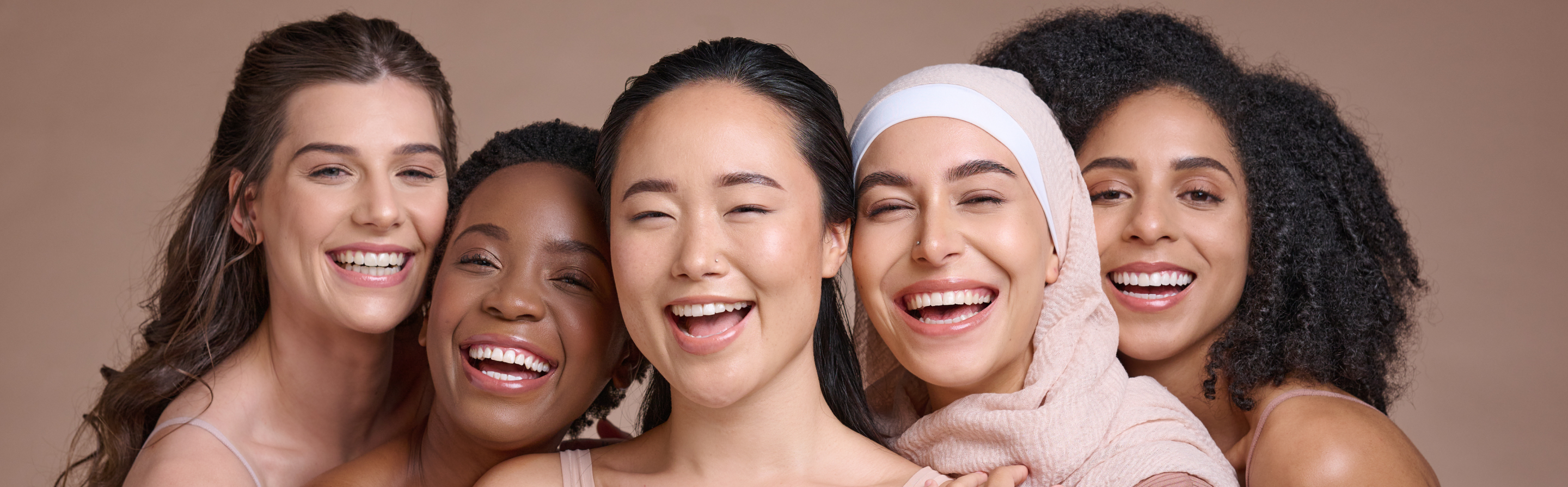 Five women of different ethnicities smiling against a beige background