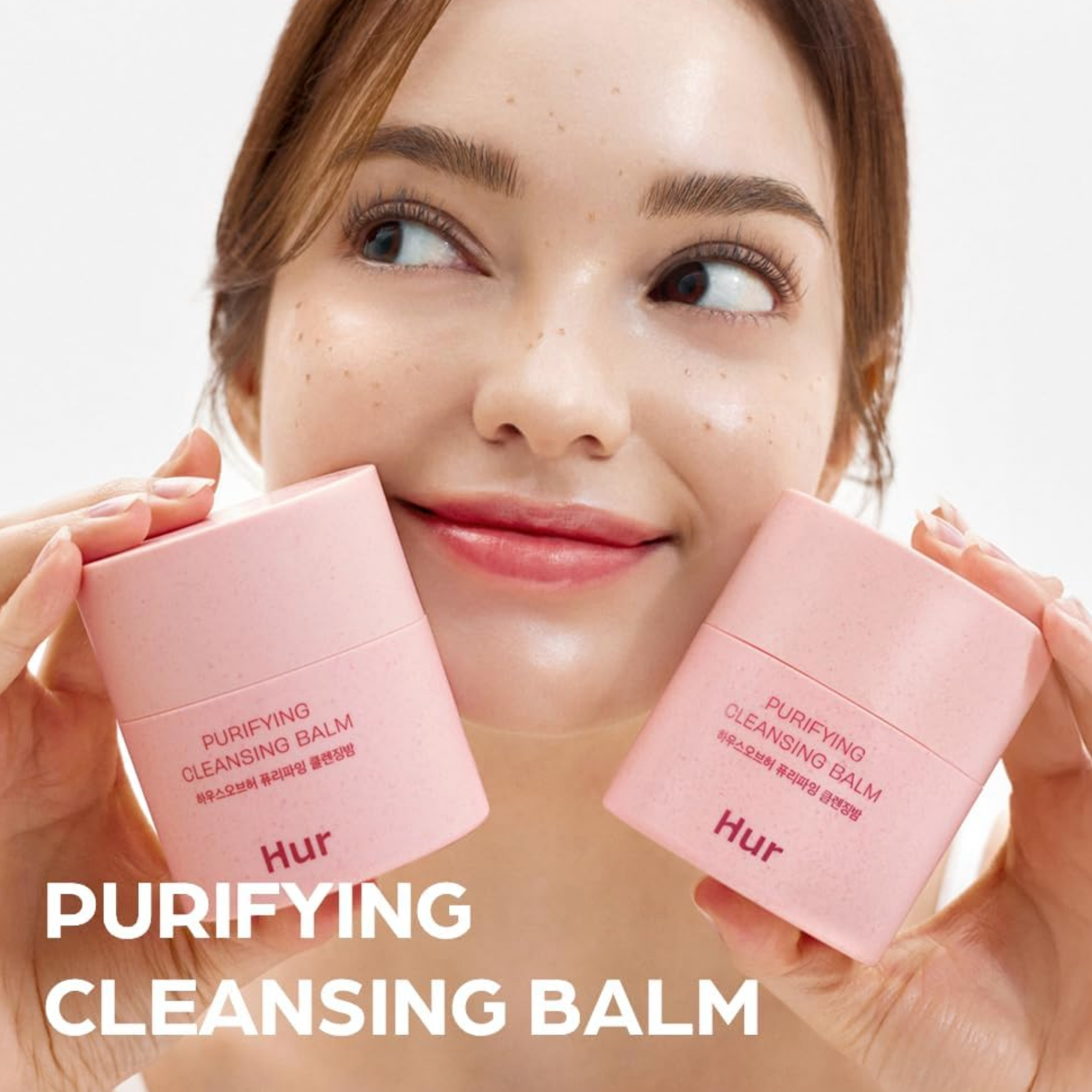 Woman holding two pink 'HUR' cleansing balms with a blurred background
