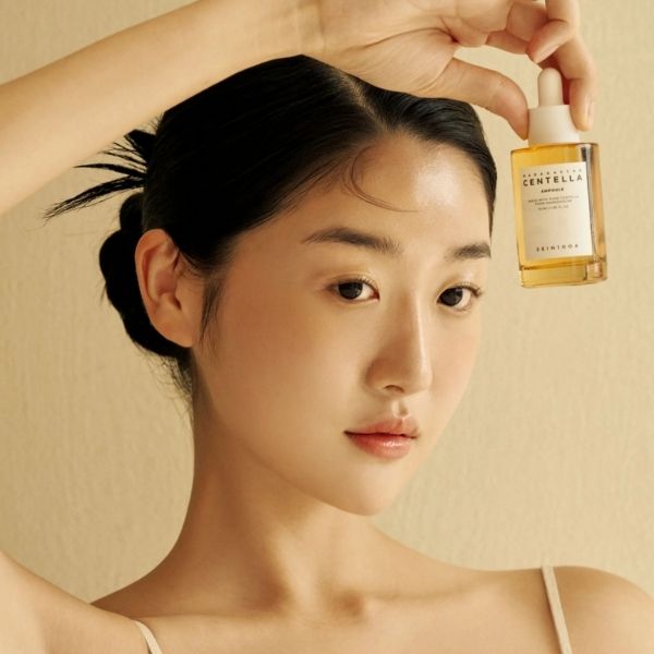 Woman holding a bottle of skincare product against a beige background